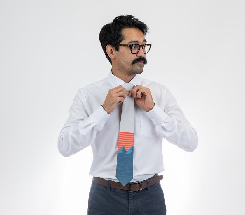A man wearing a light gray and blue mountain tie with orange and pink stripes