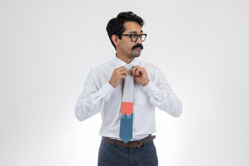 A man wearing a light gray and blue mountain tie with orange and pink stripes