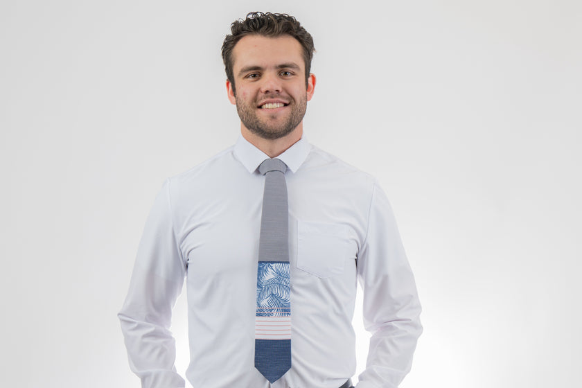 Man wearing a modern gray and blue necktie with stripes and palm leaves. Formal tie from Kator Shop Logan — refined Utah design for galas, ceremonies, and special occasions.