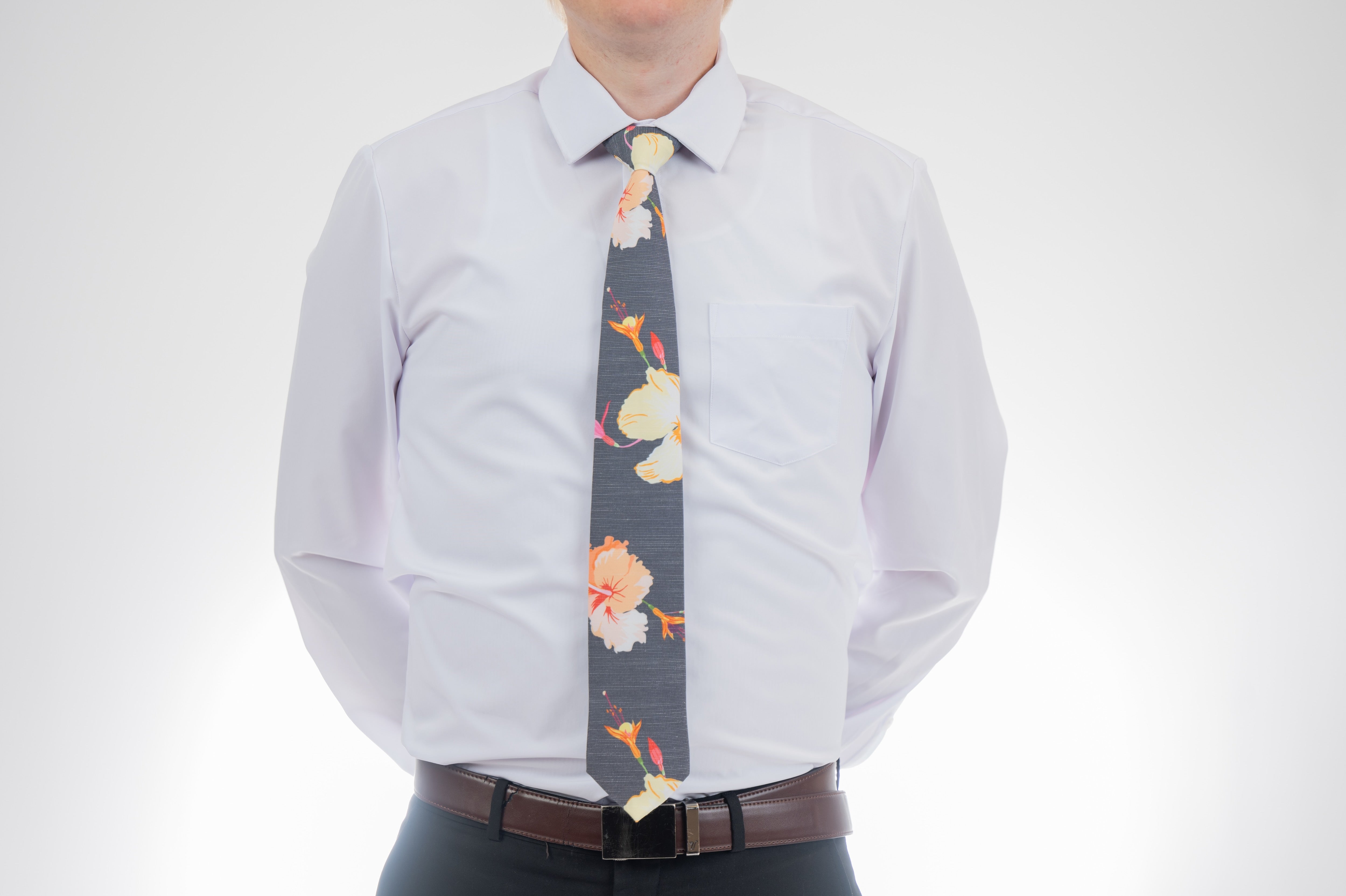 A man wearing a gray necktie with tropical floral pattern. Prom tie from Kator Shop in Logan, Utah — sleek men’s accessory for a polished, confident look on your big night.
